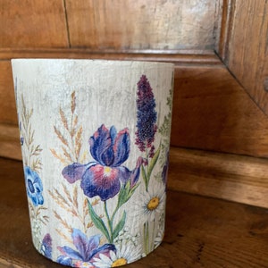 Peut inclure: Un vase cylindrique en céramique blanche avec un motif floral composé d'iris violets, de marguerites blanches et de feuillage vert.
