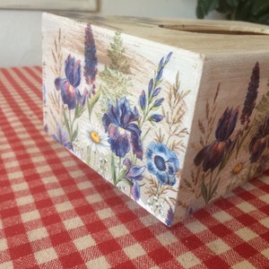 May include: A white wooden tissue box cover with a floral design featuring purple and blue irises, white daisies, and green foliage.