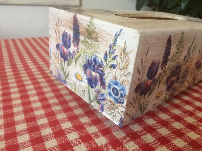 May include: A white wooden tissue box cover with a floral design featuring purple and blue irises, white daisies, and green foliage.