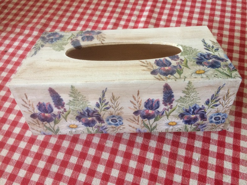 May include: A wooden tissue box cover with a floral design. The design features purple irises, white daisies, and green foliage on a white background.
