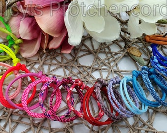 May include: A collection of colorful cord bracelets in various shades of pink, red, blue, green, and orange. The bracelets are knotted and arranged on a woven mat with floral accents. The image includes the text "Joy's Pfötchencord".