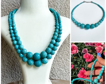 Puede incluir: Un collar de doble cadena de color turquesa azul hecho de cuentas facetadas. El collar tiene una pieza central más grande con un grupo de cuentas más grandes.
