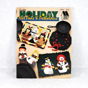May include: Crochet Holiday Hot Pads & Potholders pattern book featuring a variety of holiday-themed designs, including a snowman, pilgrims, and a wreath. The book cover is red, white, and blue with a snowflake and a bell.