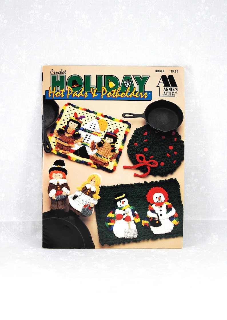 May include: Crochet Holiday Hot Pads & Potholders pattern book featuring a variety of holiday-themed designs, including a snowman, pilgrims, and a wreath. The book cover is red, white, and blue with a snowflake and a bell.