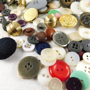 May include: A collection of assorted buttons in various colors, sizes, and materials, including plastic, metal, and fabric. Some buttons have a decorative design, while others are plain.