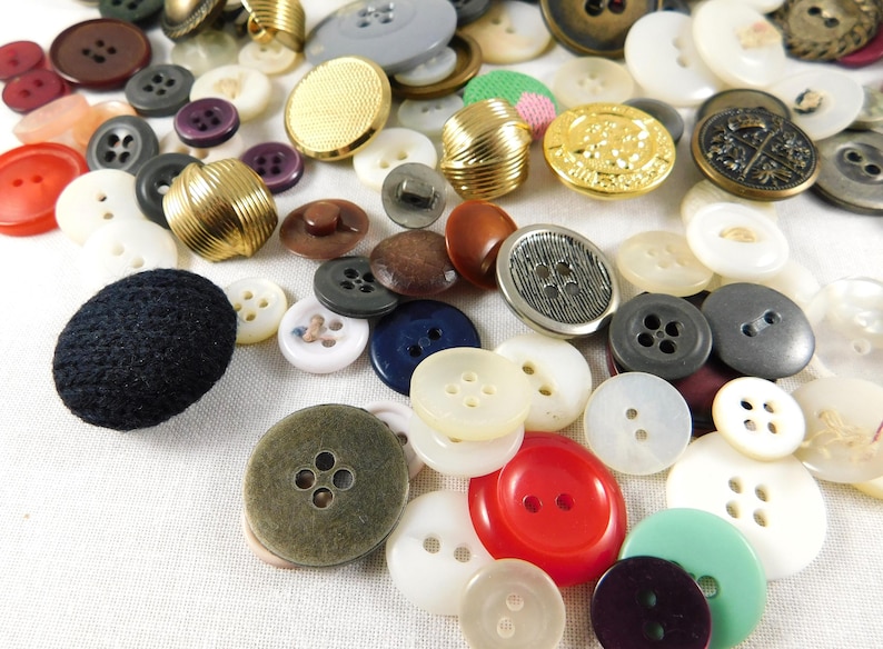 May include: A collection of assorted buttons in various colors, sizes, and materials, including plastic, metal, and fabric. Some buttons have a decorative design, while others are plain.