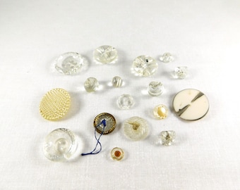 May include: Assortment of vintage buttons in various shapes, sizes, and colors, including clear glass, white, and gold. Some buttons have a textured surface.