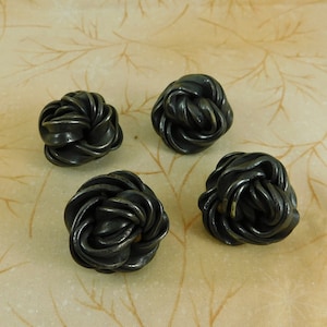 May include: Four black metal rose-shaped knobs. The knobs are made of twisted metal and have a dark, aged finish.