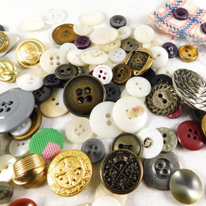 May include: A collection of vintage buttons in various colors, shapes, and sizes. The buttons are made of different materials, including metal, plastic, and fabric. Some of the buttons have intricate designs, while others are simple and plain.