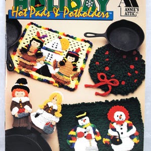 May include: Crochet Holiday Hot Pads & Potholders pattern book by Annie's Attic. The cover features a variety of crocheted designs, including a snowman, pilgrims, and a Christmas wreath.