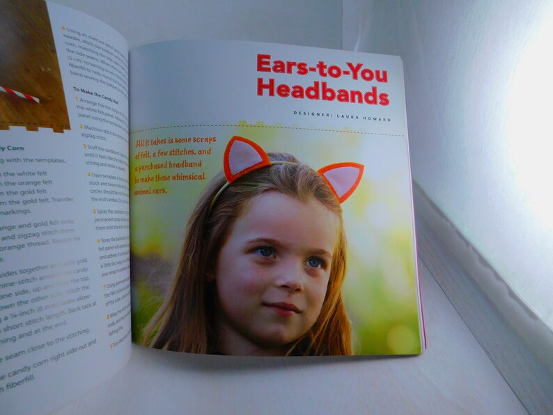 May include: A book cover with a photo of a young girl wearing a headband with orange felt ears. The title of the book is "Ears-to-You Headbands" with the designer's name, Laura Howard, listed below. The text on the page reads "All it takes is some scraps of felt, a few stitches, and a purchased headband to make these whimsical animal ears."