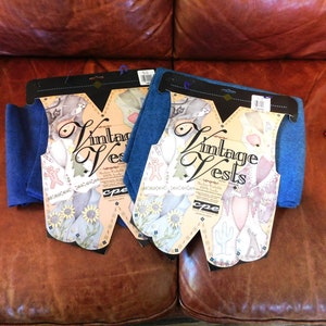 May include: Two packages of blue fabric for making vintage vests. Each package includes a pattern and instructions. The packages are labeled "Vintage Vests" and feature a whimsical design with a gingerbread man, a cactus, and a sunflower.