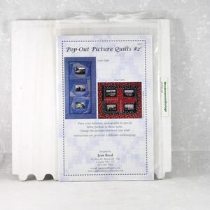 May include: A package containing a pattern for "Pop-Out Picture Quilts #2". The pattern features instructions for creating quilts with fabric pockets to display photographs. The design includes a "Crazy Quilt" and a "Log Cabin" style. The package is in a clear plastic sleeve.