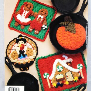 May include: Five crocheted pot holders featuring a gingerbread couple, a pumpkin, a turkey, and a gingerbread house. The pot holders are displayed on black cast iron skillets. "Printed in U.S.A." is printed on the back of the image.