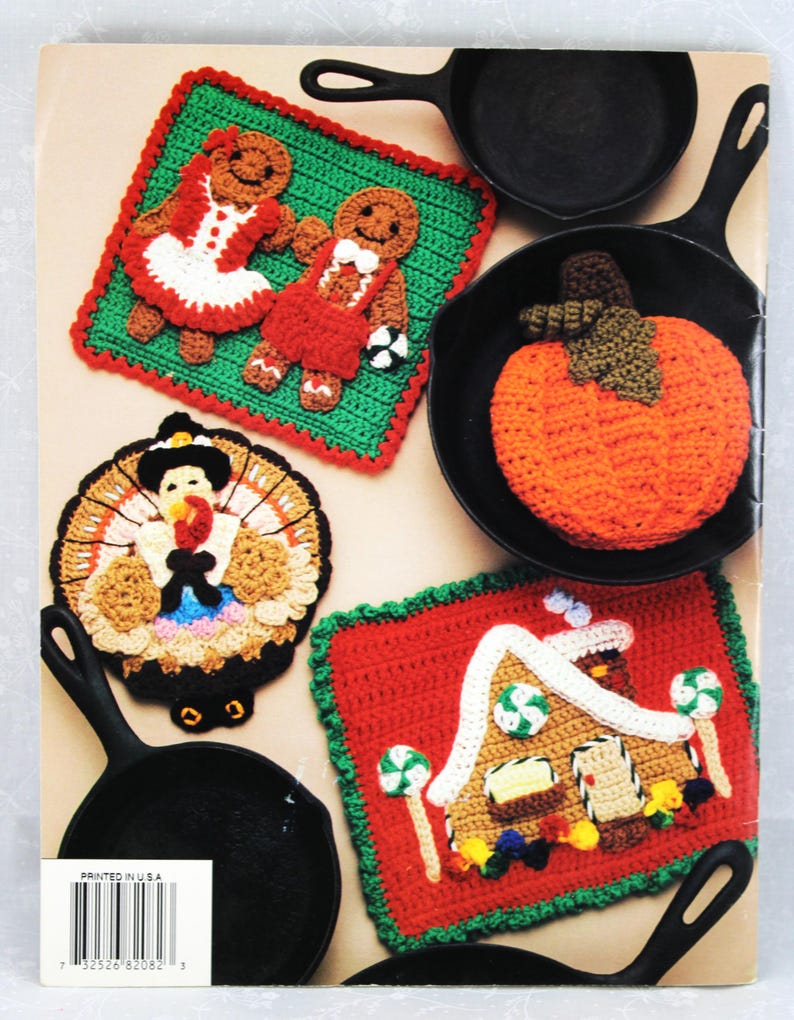 May include: Five crocheted pot holders featuring a gingerbread couple, a pumpkin, a turkey, and a gingerbread house. The pot holders are displayed on black cast iron skillets. "Printed in U.S.A." is printed on the back of the image.