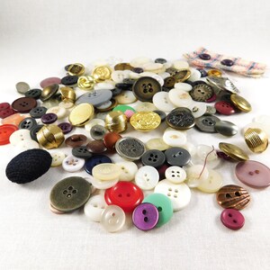 May include: A large collection of assorted buttons in various colors, shapes, and sizes. The buttons are made of plastic, metal, and fabric. Some buttons have a shiny finish, while others have a matte finish.