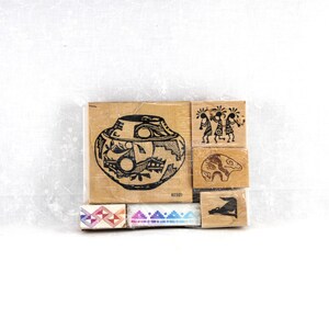 May include: A collection of six wooden rubber stamps featuring black ink designs. The largest stamp displays a patterned pottery vessel. Other stamps show three figures, a bear, a geometric border, a mountain range, and a small animal silhouette.