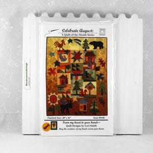 May include: A quilt kit titled "Celebrate August" from the "Quilt-of-the-Month Series." The quilt design features houses, trees, stars, and animals. Finished size is 28" x 36". Includes text: "From my heart to your hands" by Lori Smith.