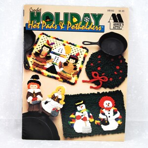 May include: Crochet Holiday Hot Pads & Potholders pattern book featuring a variety of designs including a snowman, pilgrims, and a Native American family. The book cover is red, white, and blue with a snowflake and a bell.