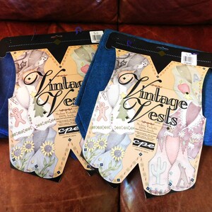 May include: Two packages of vintage vests, each with a blue felt backing and a colorful illustration of a vest with a gingerbread man, a tree, and a cactus. The packages are labeled "Vintage Vests" and "Machine Washable 100% Acrylic".