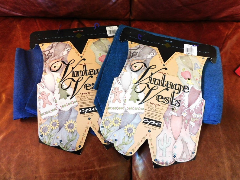 May include: Two packages of vintage vests, each with a blue felt backing and a colorful illustration of a vest with a gingerbread man, a tree, and a cactus. The packages are labeled "Vintage Vests" and "Machine Washable 100% Acrylic".