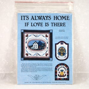 May include: A package containing a quilt pattern with the text "IT'S ALWAYS HOME IF LOVE IS THERE." The design includes a house, floral elements, and the word "WELCOME." The package is in a clear plastic bag.