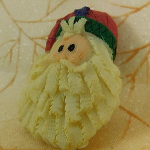 Peut inclure: Une petite figurine en c&eacute;ramique blanche de P&egrave;re No&euml;l avec un chapeau rouge, une garniture verte et une barbe blanche. La figurine est d&eacute;taill&eacute;e avec une barbe textur&eacute;e et des yeux peints.
