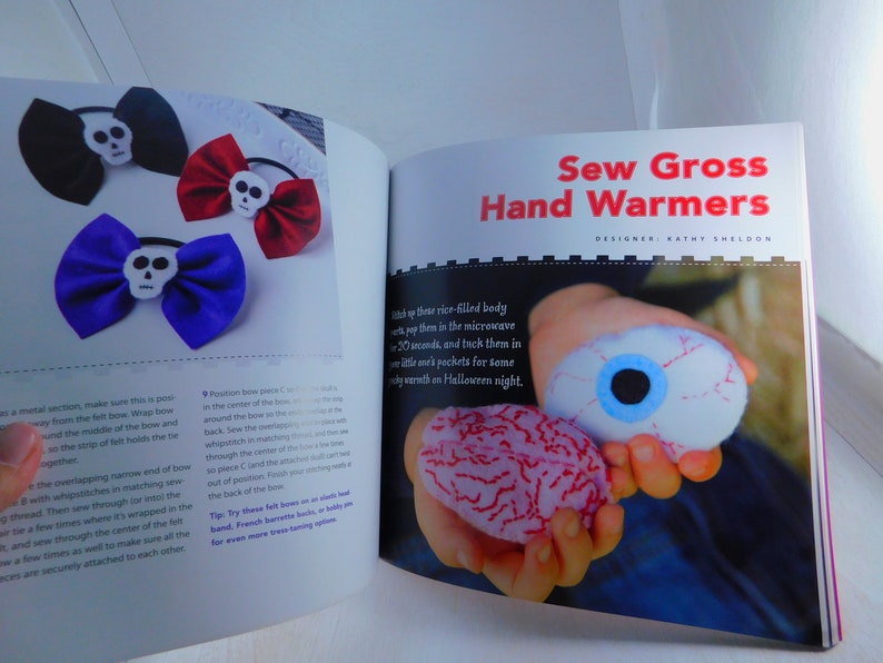 May include: A book titled "Sew Gross Hand Warmers" with a photo of a child holding two hand warmers shaped like an eyeball and a brain. The book is open to a page with instructions on how to make the hand warmers.