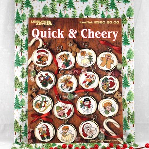 May include: A Christmas-themed craft leaflet titled "Quick & Cheery" featuring cross-stitch designs. The cover displays various round ornaments with festive images like Santa Claus and snowmen. The background has a Christmas tree pattern.