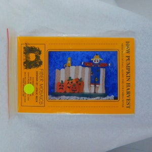 May include: A yellow pattern sheet for a fiber mosaic craft project called "106W Pumpkin Harvest". The pattern features a scarecrow, pumpkins, and a cat. The pattern is by Fiber Mosaics Designs by Leslie Beck.