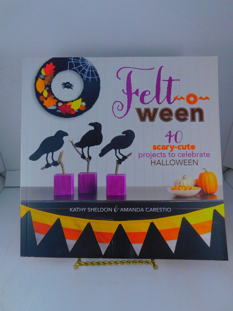 May include: Book cover with the title "Felt Ween" and the subtitle "40 scary-cute projects to celebrate HALLOWEEN". The cover features a felt wreath with a spider, three black felt crows, and a felt candy corn garland.