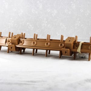 May include: A brown plastic object with multiple rectangular and cylindrical components. The object has several vertical posts and circular details. It is secured with a tan elastic band. The item is likely a component of a larger structure.