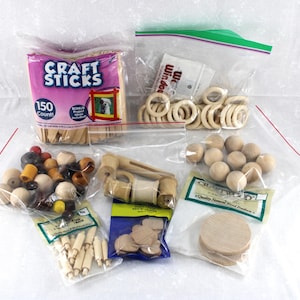 May include: Assortment of craft supplies in clear plastic bags. Includes wooden craft sticks, beads, rings, balls, and other wooden shapes. The craft sticks are in a pink package with the text "Craft Sticks".