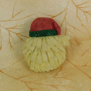 Peut inclure: Une petite figurine en c&eacute;ramique blanche de P&egrave;re No&euml;l avec un chapeau rouge et vert. La figurine a une barbe d&eacute;taill&eacute;e et est parfaite pour la d&eacute;coration des f&ecirc;tes.