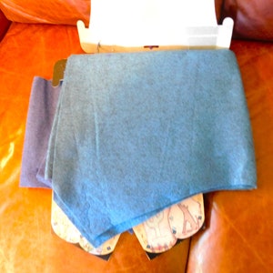 May include: Two scarves, one blue and one dark purple, folded and displayed on a brown leather surface. The blue scarf is folded on top of the purple scarf.