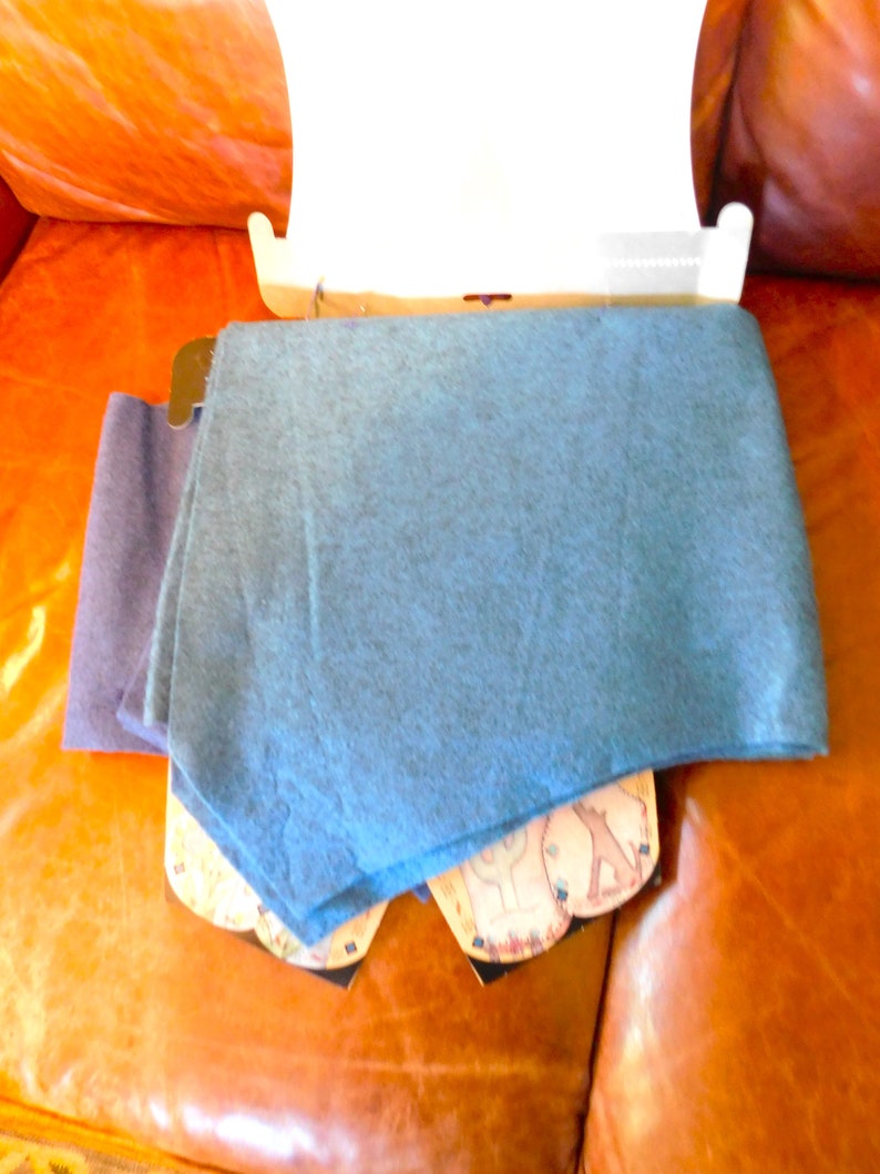 May include: Two scarves, one blue and one dark purple, folded and displayed on a brown leather surface. The blue scarf is folded on top of the purple scarf.