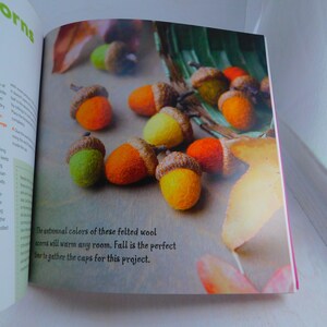 May include: Close-up of felt acorns in various autumnal colors, including orange, yellow, and green. The text "The autumnal colors of these felted wool acorns will warm any room. Fall is the perfect time to gather the caps for this project." is visible in the image.