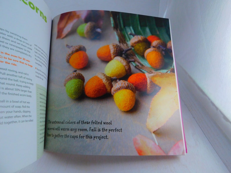 May include: Close-up of felt acorns in various autumnal colors, including orange, yellow, and green. The text "The autumnal colors of these felted wool acorns will warm any room. Fall is the perfect time to gather the caps for this project." is visible in the image.