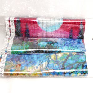 May include: Three rolled diamond painting kits, each wrapped in clear plastic. The top kit features a red and pink landscape with a light blue moon. The middle kit has a blue and green design, and the bottom kit has a blue and yellow design.