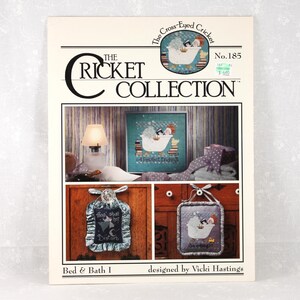 May include: A catalog cover for "The Cricket Collection" featuring cross-stitch patterns. The design includes a central image of a duck in a bathtub, with additional cross-stitch examples below. The text includes "Bed & Bath I" and "designed by Vicki Hastings."