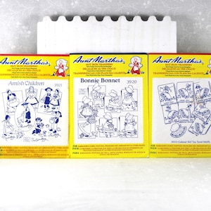 May include: Three yellow and white Aunt Martha's hot iron transfer packets featuring blue line art designs. The left packet is labeled Amish Children, the center is Bonnie Bonnet, and the right is Colonial Girl Tea Towel Motifs.