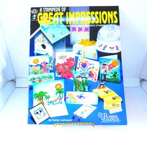 May include: A book titled "A Stampede of Great Impressions" with a blue cover and colorful illustrations of rubber stamped images. The book is about tips and techniques for using rubber stamps. The book is by Karen Johnson.