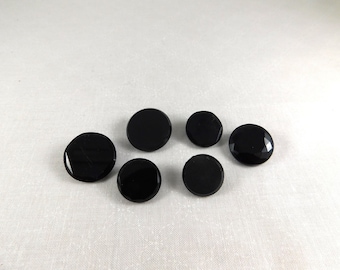 May include: Six black round buttons with a shiny finish. The buttons are arranged in a semi-circle on a white surface.