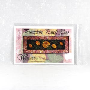 May include: A sewing pattern packet titled Pumpkin Patch Too by Wildfire Designs Alaska. The cover features a rectangular illustration of orange pumpkins on a black background with green vines, surrounded by a pink and orange floral border.