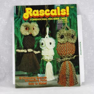 May include: A vintage craft instruction booklet titled Rascals! 3-DIMENSIONAL MACRAME OWLS by Diane Best. The cover features three macrame owl wall hangings in brown, white, and green tones, each perched on a small branch with hanging tassel details.