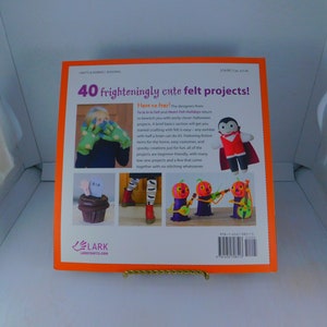 May include: The back cover of a book titled "40 frighteningly cute felt projects!"  The book features a bright orange background with a variety of felt projects, including a vampire, a ghost, and a cupcake. The book is published by Lark Crafts.