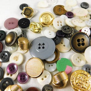 May include: A large collection of assorted buttons in various colors, shapes, and sizes. The buttons are made of different materials, including metal, plastic, and fabric. Some buttons have intricate designs, while others are simple and plain.