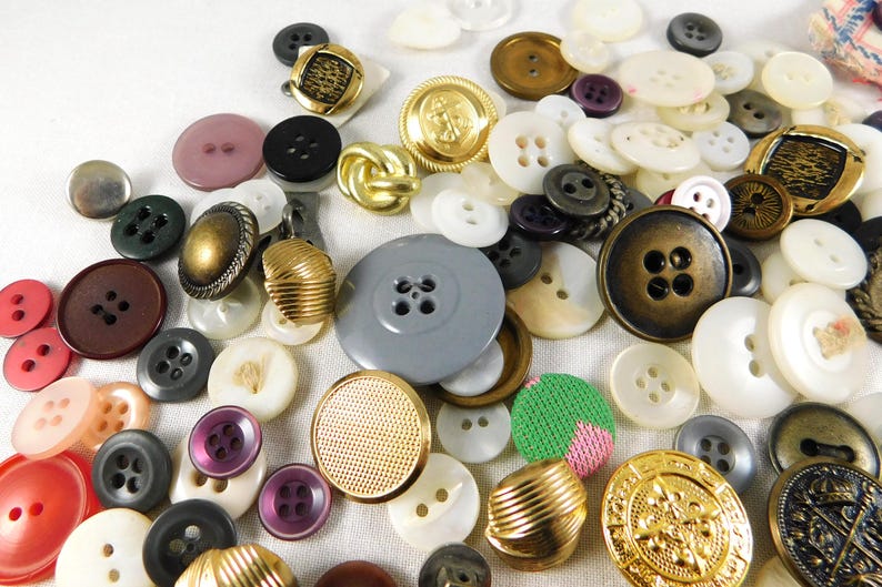 May include: A large collection of assorted buttons in various colors, shapes, and sizes. The buttons are made of different materials, including metal, plastic, and fabric. Some buttons have intricate designs, while others are simple and plain.