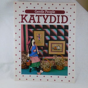 May include: A cross-stitch pattern booklet titled "Gentle People KATYDID" featuring a colorful illustration of a girl holding a fishing pole and a basket of flowers. The illustration is surrounded by a white border with a red diamond pattern.