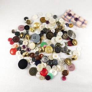 May include: A large collection of assorted buttons in various colors, sizes, and materials, including plastic, metal, and fabric. The buttons are arranged in a random pattern on a white surface.